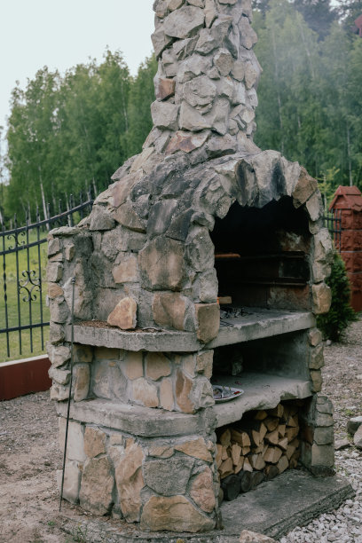 石头烧烤在花园与防火栅栏和植物的背景。图片下载