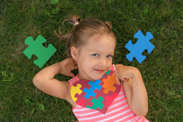 一个学龄前儿童躺在草地上，周围都是带着心形卡片的拼图图片下载