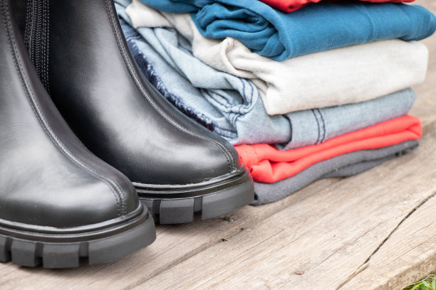 女式厚底黑高筒靴和一堆东西站在一块木板上晒在街上，女式的鞋子和冬装，时髦的衣服和鞋子图片下载