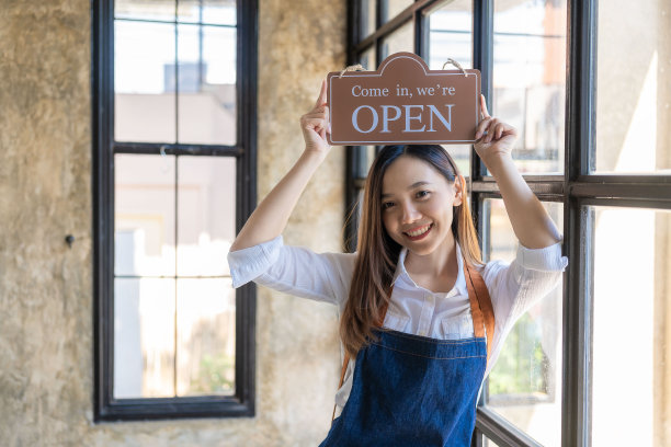 微笑的小女企业家拿着开放的标志小企业主微笑着改变开放地点的标志女人拿着标志我们现在正在开设一个当地的支持业务。图片下载