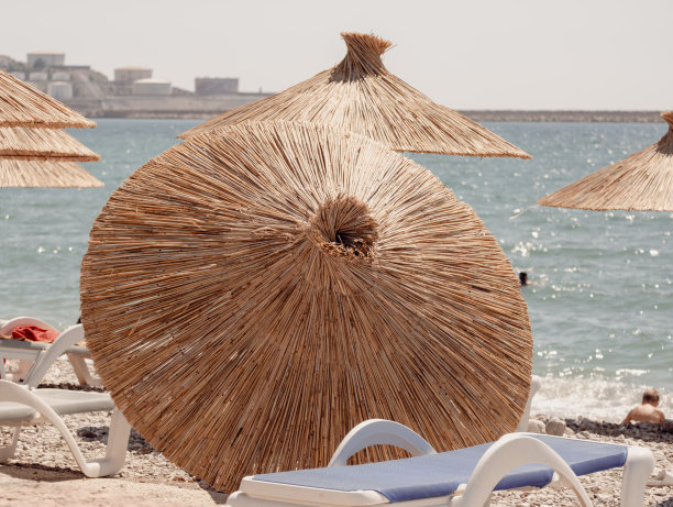 阳光明媚的一天。一把落在沙滩上的竹伞图片下载