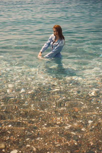 一个穿着及腰牛仔连身裤的女孩站在海水中，半转身对着镜头图片下载
