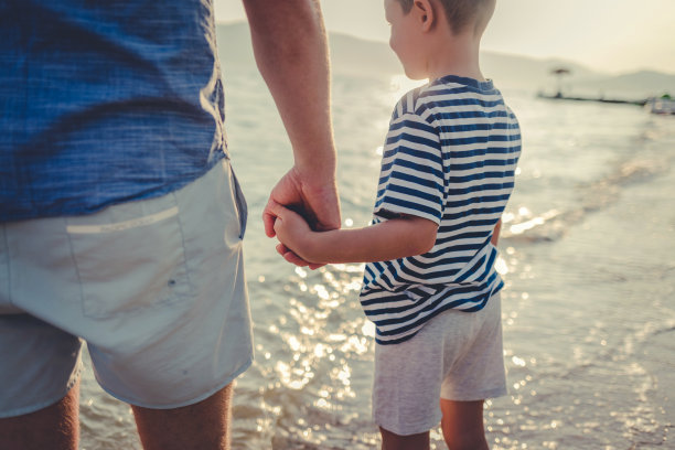 白人父亲和儿子在海滩上散步的照片。一个快乐的小男孩和他的父亲在海滩上享受一天。图片下载