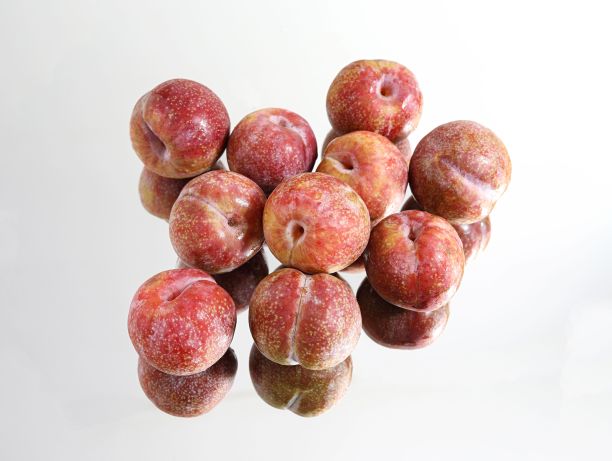 各种成熟的红李子在反光的白色表面上的特写图片下载