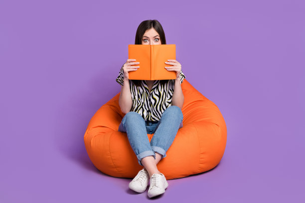 印象深刻的女孩的全尺寸肖像坐舒适的袋子持有打开的书封面脸孤立的紫色背景图片下载