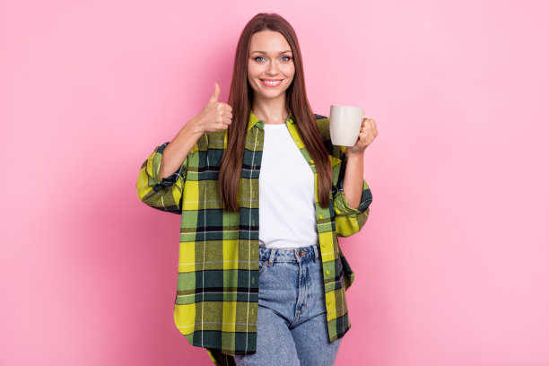开朗满意的直发女孩的肖像，穿着格子衣服，拿着可可杯，在粉红色的背景上显得很孤立图片下载