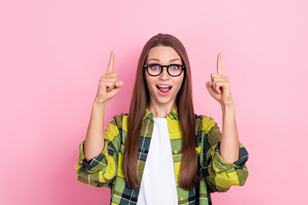 照片中，惊讶而欢快的女士张开嘴，手指直接指向粉红色背景上的空白空间图片下载