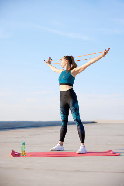 有力的手。年轻的运动妇女在时尚的运动服训练健身松紧带在温暖的阳光明媚的户外图片下载