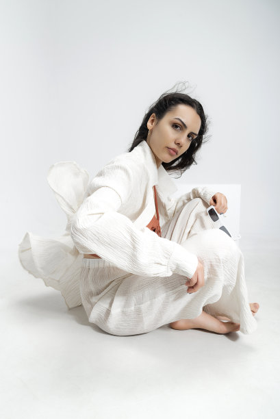 年轻美丽的照片模特穿着薄织物，夏天的白衬衫和白裤子，在白色背景的工作室里摆出艺术的姿势。图片下载