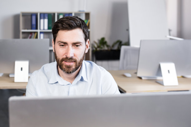 一个年轻人，一名办公室职员坐在办公室的办公桌前，对着电脑摄像头进行视频通话，与合作伙伴、客户讨论工作。图片下载