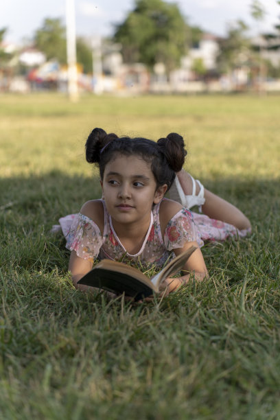 女孩在绿色的田野里看书。图片下载