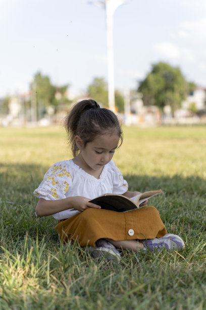 女孩在绿色的田野里看书。图片下载