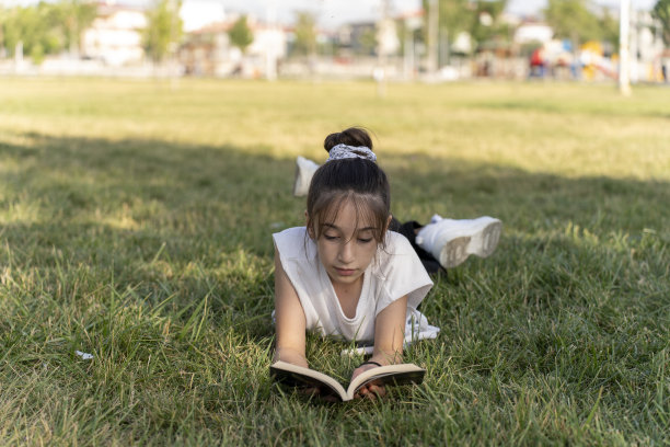 女孩在绿色的田野里看书。图片下载