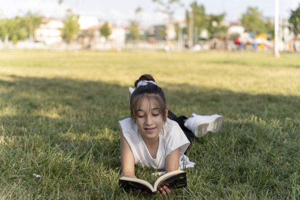 女孩在绿色的田野里看书。图片下载