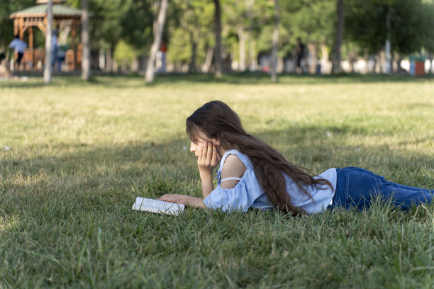 女孩在绿色的田野里看书。图片下载