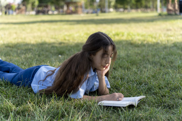 女孩在绿色的田野里看书。图片下载