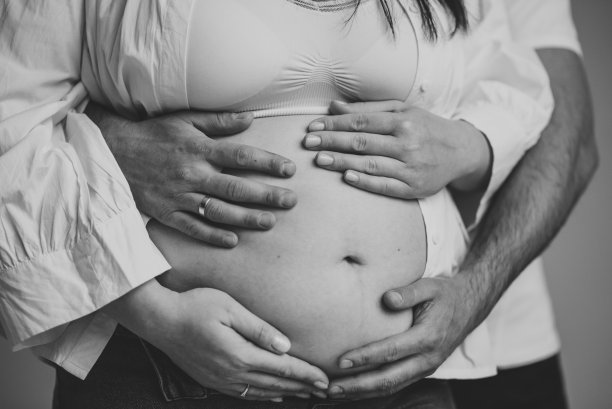 爱的夫妻。丈夫把手放在怀孕妻子的肚子上。怀孕的女人，可爱的帅哥在家里抱着肚子。亲子关系的概念。等待宝贝。九个月的特写。黑白照片图片下载