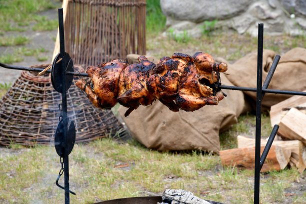 在中世纪的节日或集市上，在田野或草地旁的木制炉子或带有金属框架的烤箱上，近距离拍摄一只美味的鸡肉，经过蒸煮和烘烤图片下载