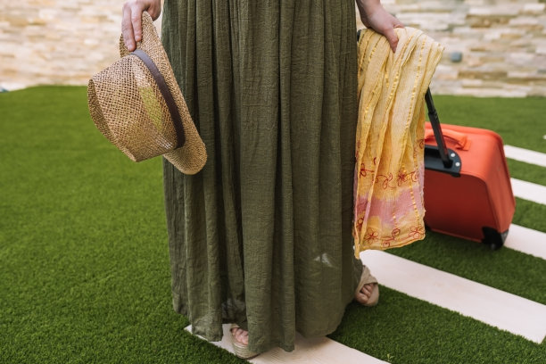 一个年轻女人的镜头，进入酒店前台，她的行李箱上了轮子。一个女人穿着夏天的衣服去旅行。图片下载