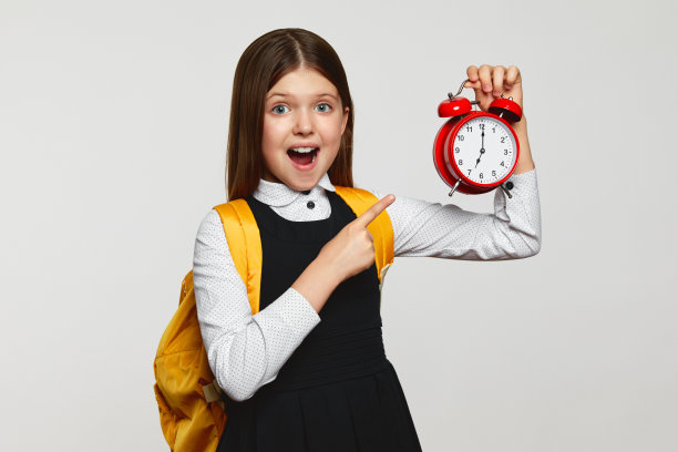 震惊的女学生一边看着镜头，一边用手指着经典的红铃闹钟图片下载