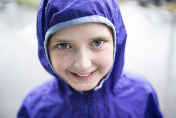 在夏天的雨中，一个穿着紫色雨衣的微笑男孩的肖像图片下载