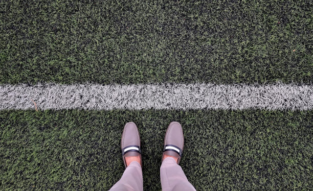 穿着棕色复古休闲鞋和米色休闲裤的商人。年轻的商人放松地站在绿色的草地上，排成起跑线。男人腿的特写开始概念。图片下载