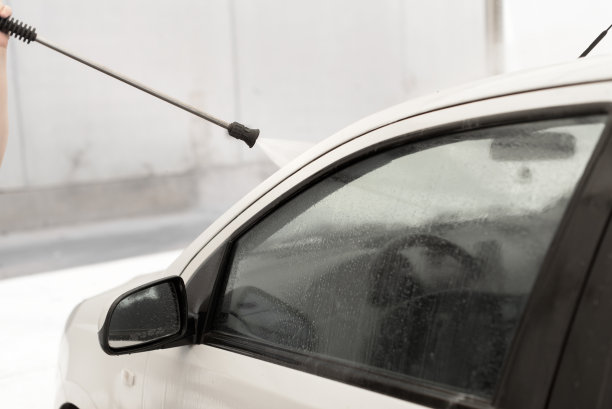 在自助洗车店用高压软管喷枪清洗白色汽车。图片下载