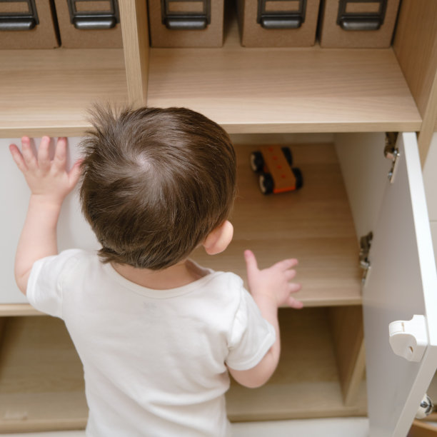 蹒跚学步的婴儿打开家里客厅的壁橱门。一个小孩打开架子上的抽屉。一岁八个月的孩子图片下载