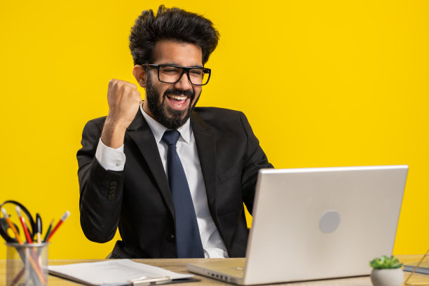 商人中奖工作浏览打字在办公室的笔记本电脑上庆祝大彩票赢得了好消息图片下载