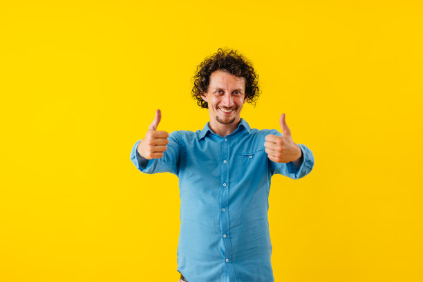 竖起大拇指的快乐年轻人站在一堵黄墙前图片下载
