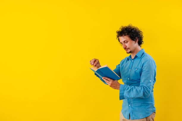 一个年轻人在一堵黄墙前看书图片下载