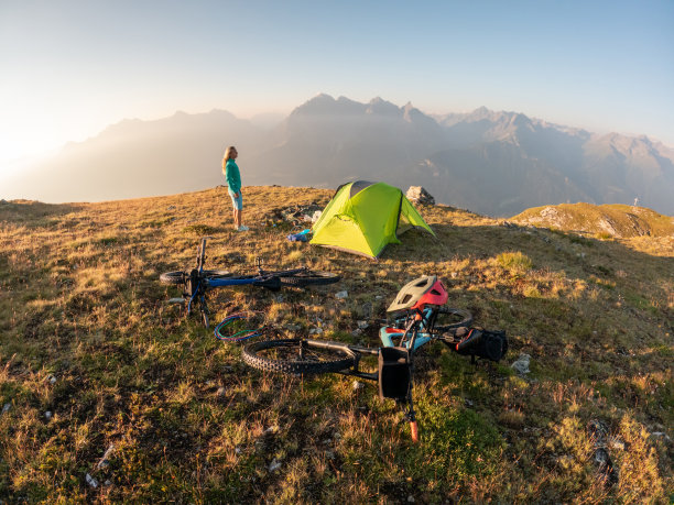 女人骑着自行车打包和露营，她在山顶搭起帐篷，日落时分图片下载