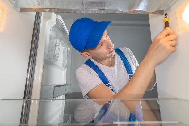 穿着工作服的男技术员用螺丝刀修理坏了的冰箱。冰箱维修的概念。冰箱里面的照片图片下载