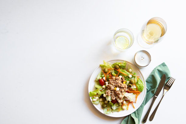 餐桌设置的俯视图，经典的金枪鱼沙拉与不同的生菜，白葡萄酒杯，水和胡椒壶。复制空间图片下载