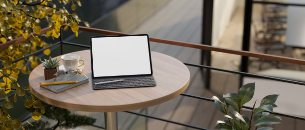 一个带无线键盘的数字平板电脑，放在家里阳台的木制圆桌上。图片下载