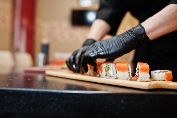 专业厨师戴着黑色手套的近距离双手在日本传统食品的餐厅厨房制作寿司和卷。图片下载