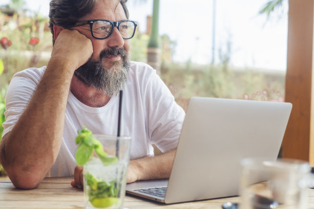 一个男人放松地看着酒吧，在桌子上放着电脑和鸡尾酒。暑假假期旅游和数字游牧民工作者工作生活方式的人。安详的表情男性年龄图片下载