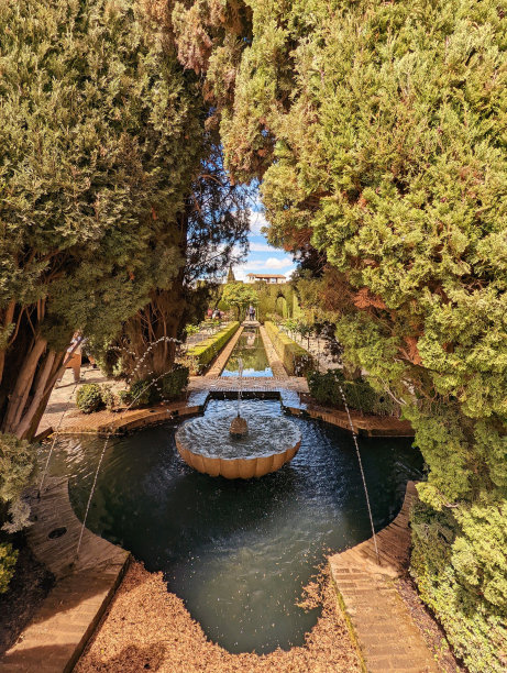 壮观的喷泉周围葱郁的绿色植物在西班牙阿尔罕布拉花园沐浴阳光图片下载