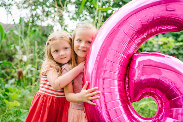 快乐的姐妹，女孩朋友，抱着气球在后院庆祝六岁生日。有趣的情绪化的孩子们在花园里拿着粉红色的气球。6岁，6岁生日聚会庆祝。图片下载