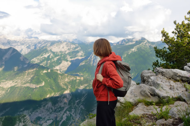徒步旅行时，女徒步者站在山谷的石坡上的侧视图。年轻女子在阿尔卑斯山徒步旅行时欣赏着风景如画的岩石山峰图片下载