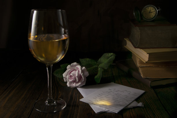 照片中，黑色的背景是一杯酒，上面有一封信和一朵玫瑰，还有书和一个时钟图片下载