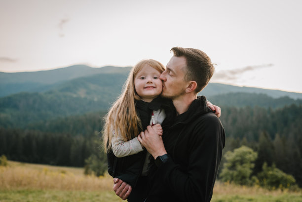 日落时分，孩子抱着父亲在公园里玩耍。友好家庭的概念。父亲节。照片中的爸爸和女儿在山上的夏天和秋天的假期。放文字的地方。特写镜头。图片下载