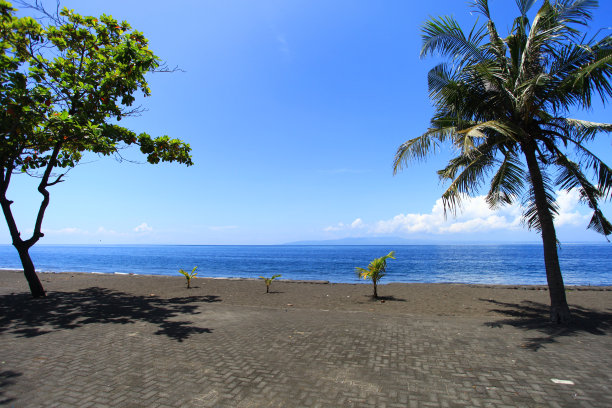 果阿拉瓦海滩在巴厘岛的一个空的黑色沙滩，椰子树，蓝天，蓝色的大海和努沙伦邦根岛在地平线上。眼前一个人也没有。图片下载