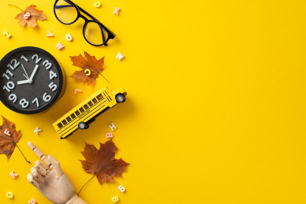 准备去上学。在生动的黄色背景下，人体模型手指示字母、眼镜、校车玩具和闹钟的俯视图。有足够的空间存放你的信息图片下载