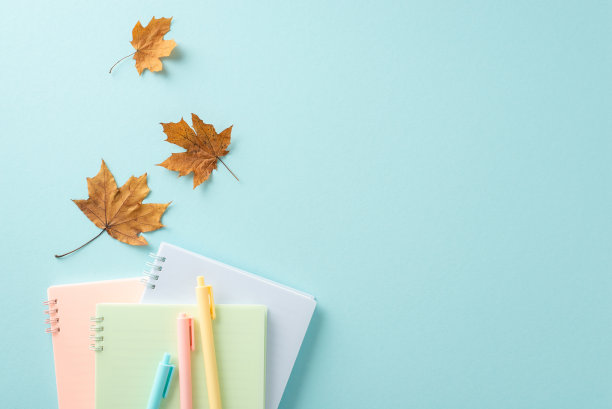回到学校的概念。高角度视角的创意照片，具有丰富多彩的笔记本和笔与枫叶在平静柔和的蓝色背景与文字或广告的复制空间图片下载