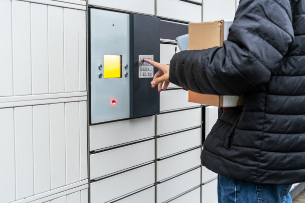 在自助邮件终端机附近，一名男子手里拿着一个盒子。包裹投递机。拿着纸板箱的人。邮件投递和邮政服务，网上购物，电子商务的概念图片下载