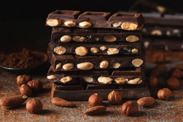 黑巧克力和牛奶巧克力，坚果在深色背景上撒上可可粉。图片下载