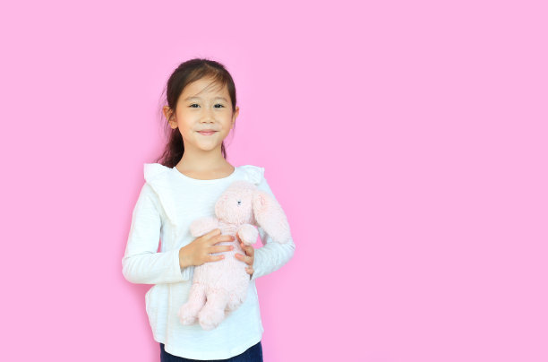 美丽的亚洲儿童女孩抱着粉红色的毛茸茸的兔子娃娃孤立在粉红色的背景与复制空间。复活节快乐的孩子。图片下载
