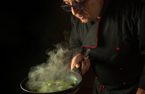 在厨房里煮新鲜蔬菜。厨师手里拿着热气腾腾的平底锅。酒店广告位的亚洲美食创意图片下载