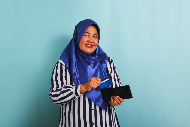 戴头巾的中年亚洲妇女从钱包里拿出信用卡，在蓝色背景中孤立图片下载